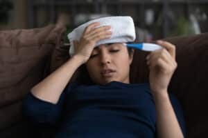 Young woman holding head and looking at thermometer