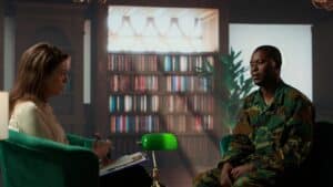 American veteran in camouflage uniform sits across from a counselor in a dimly lit room