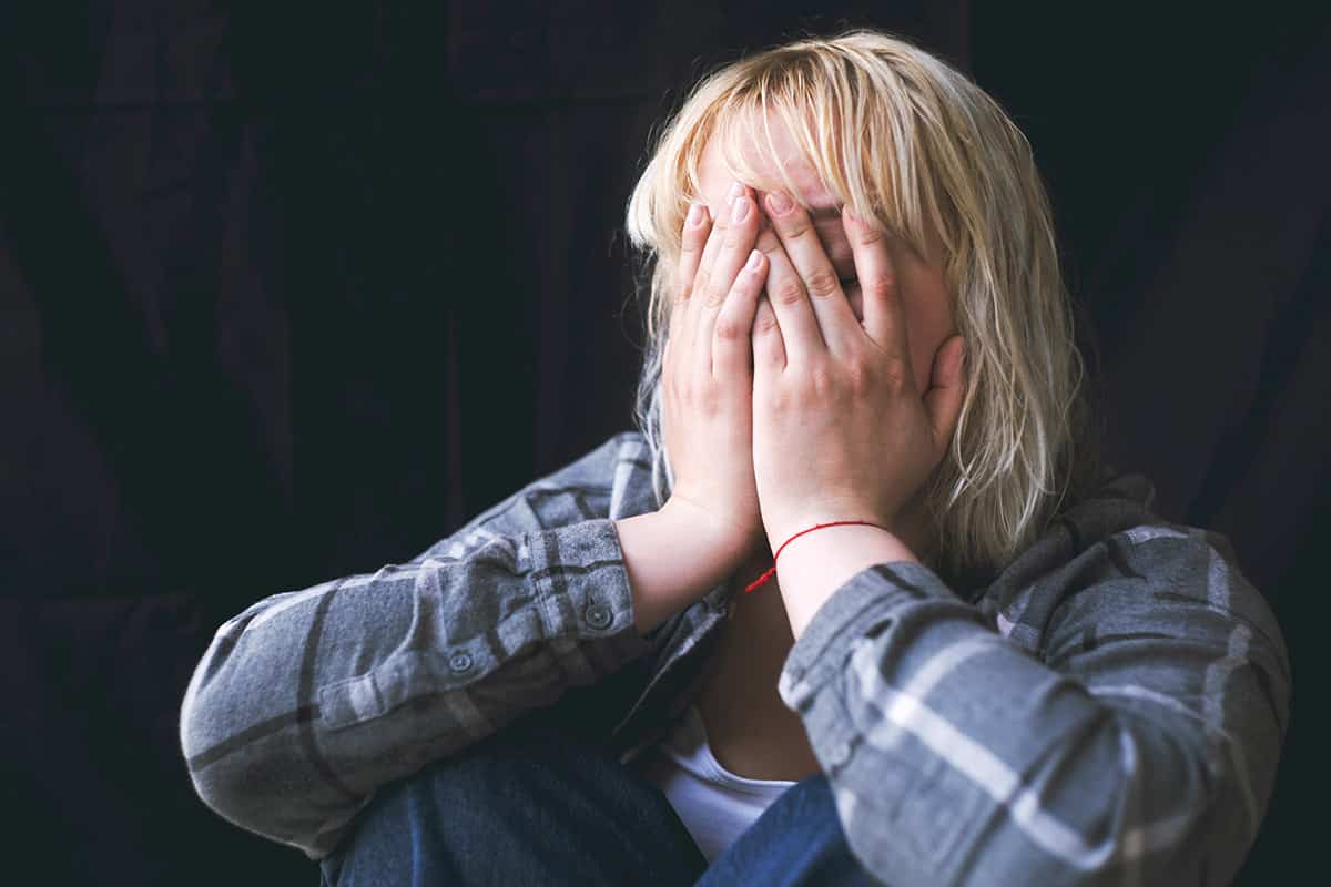Young woman sitting alone in dark room covering her face with her hands, depicting mental health struggles
