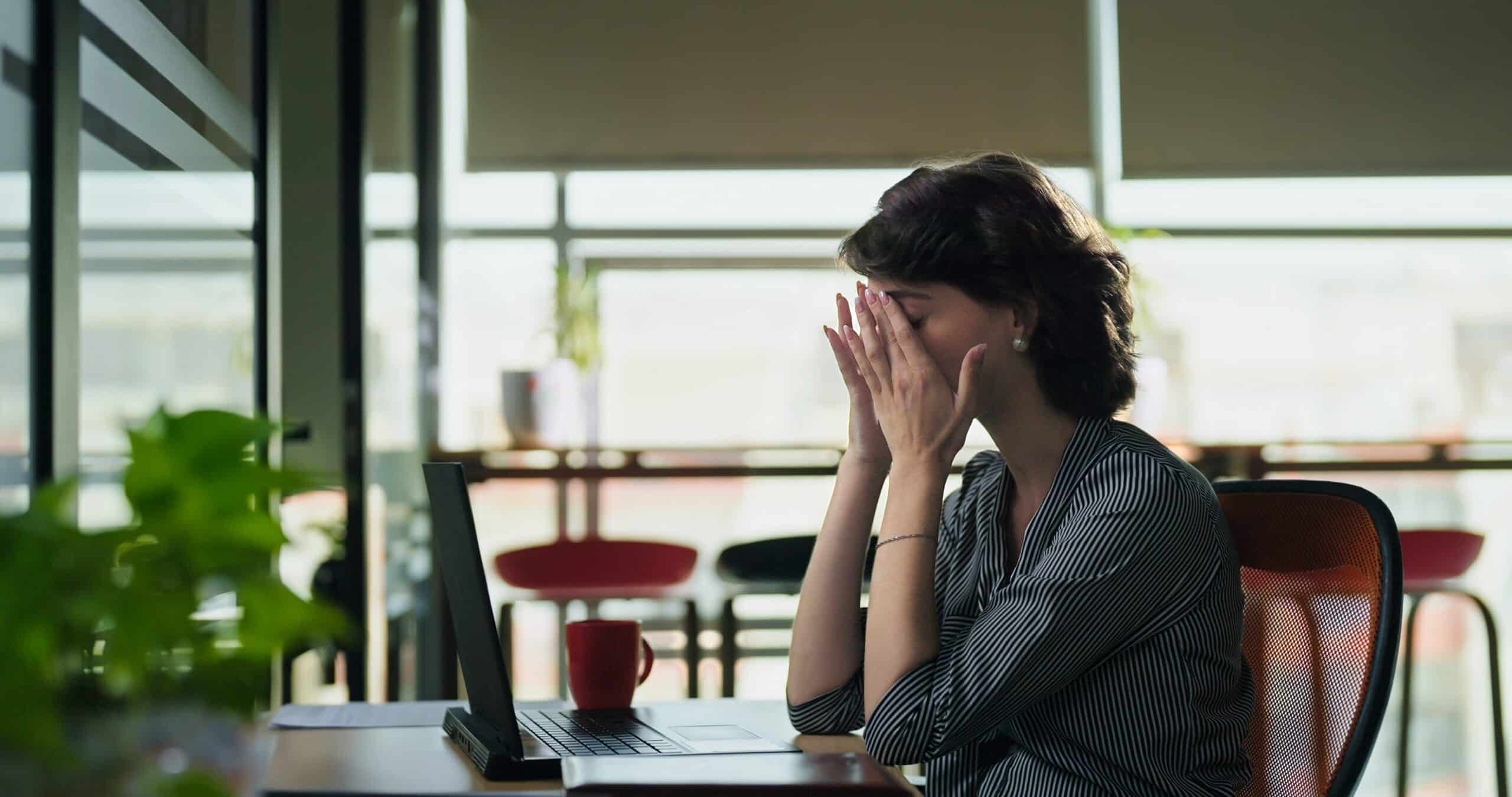 Young gen z woman rubbing her eyes at desk with her laptop, appearing tired at work