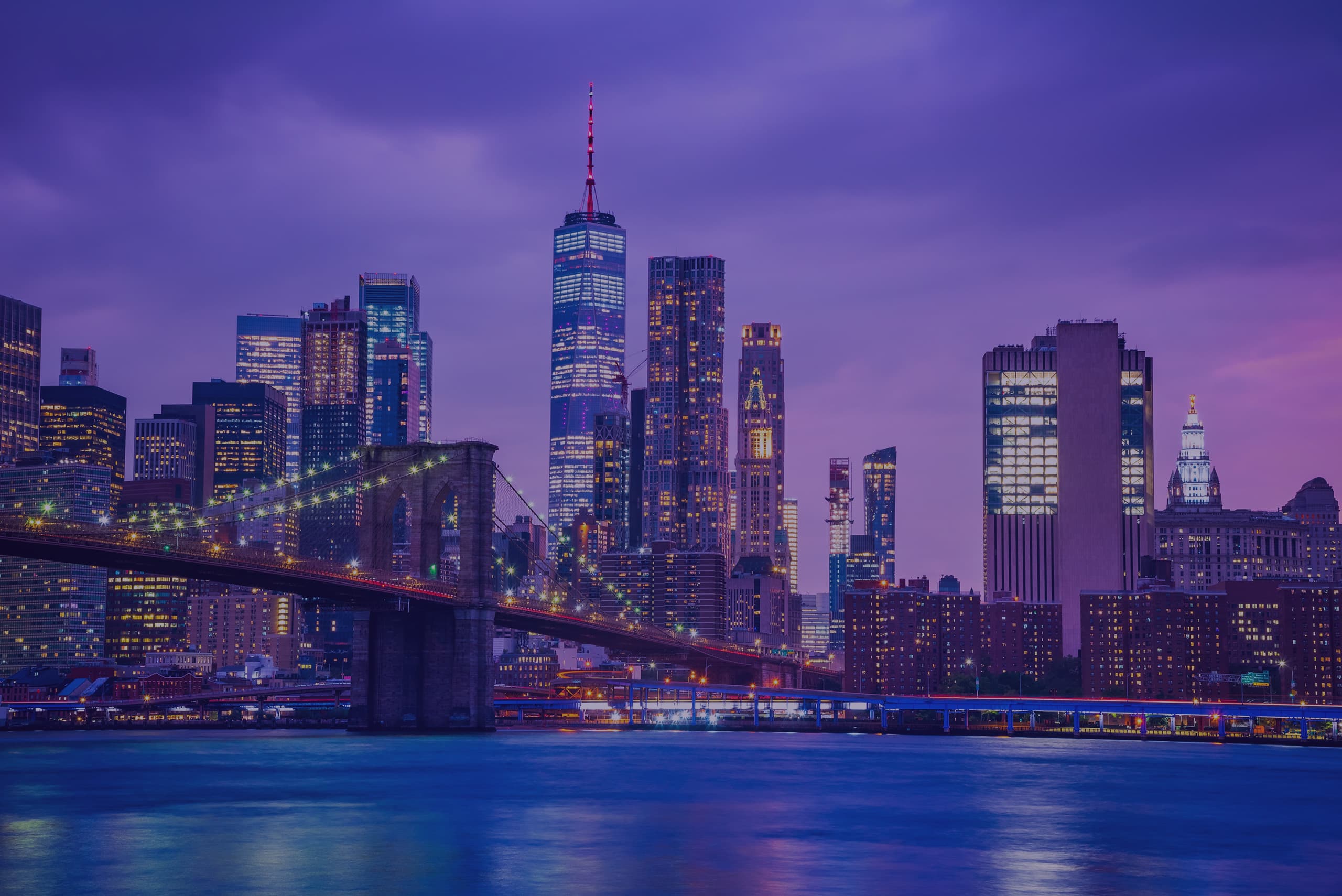 Brooklyn Bridge spanning the East River with Manhattan skyline in the background under a clear blue sky.