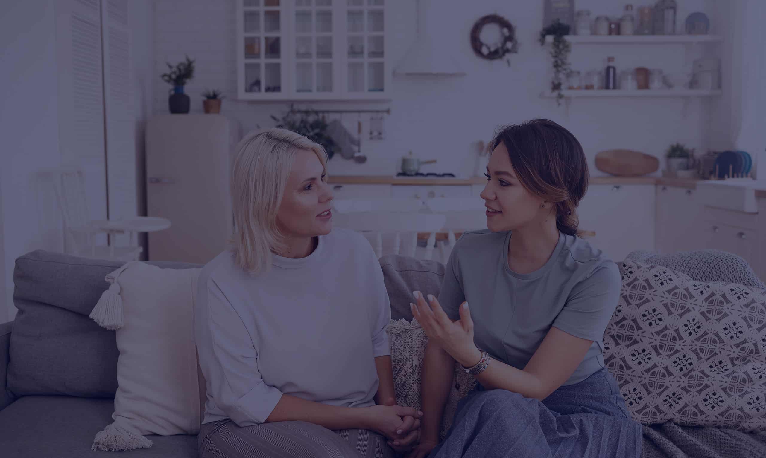 Mother and adult daughter having a conversation while sitting on a sofa.