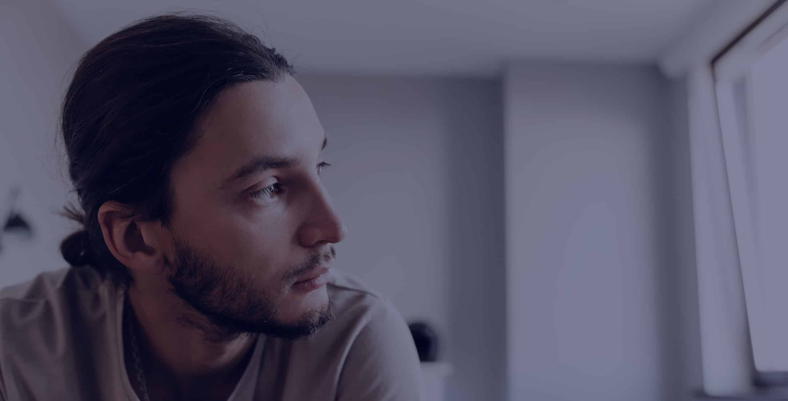 Depressed man sitting on his bed and looking out his window