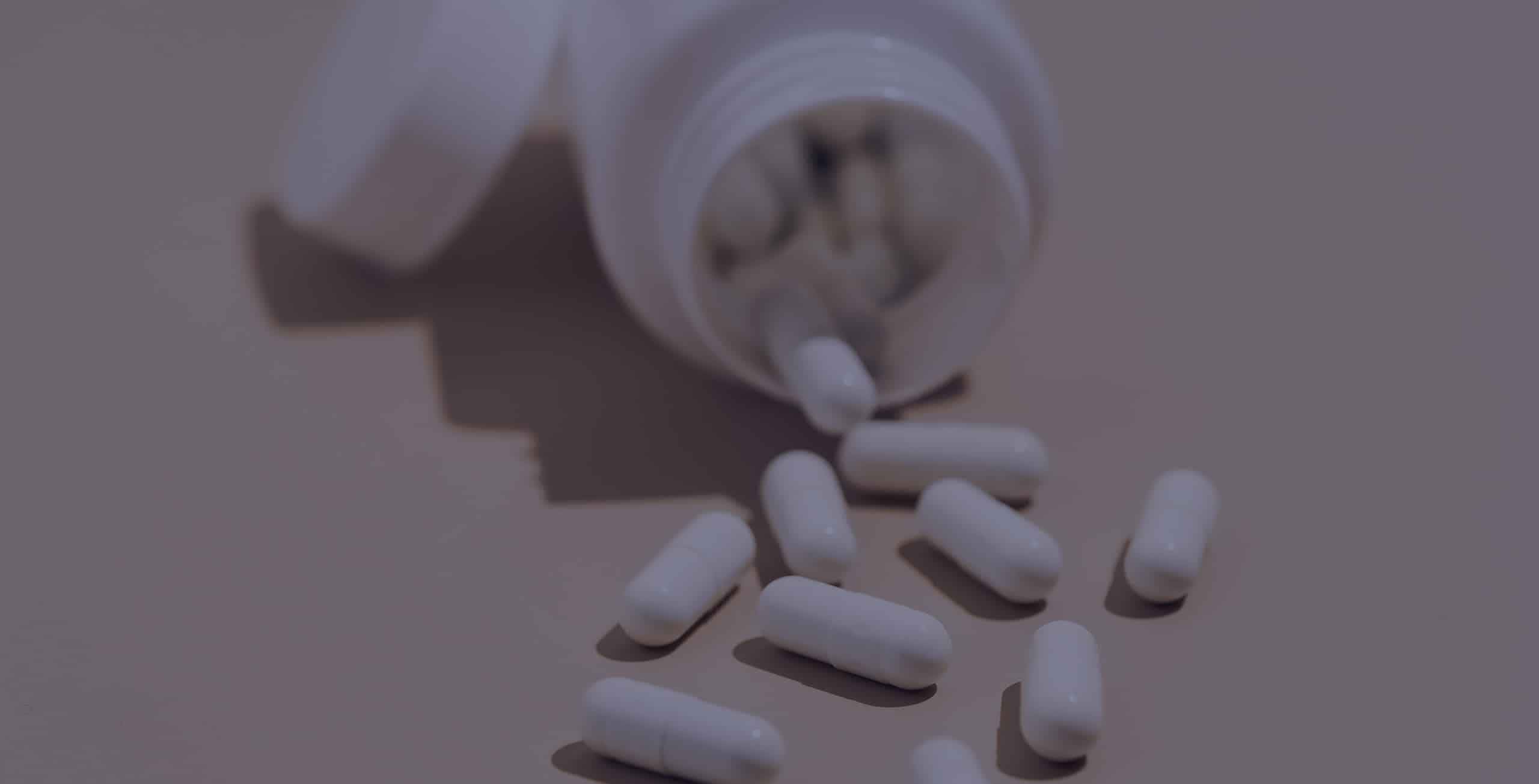 Close-up of white capsule pills spilling out of a plastic jar on a beige isolated background.